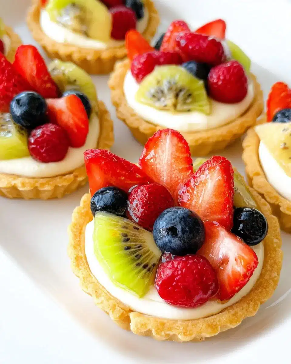 Delicious mini fruit tarts topped with fresh fruits and cream on a buttery crust